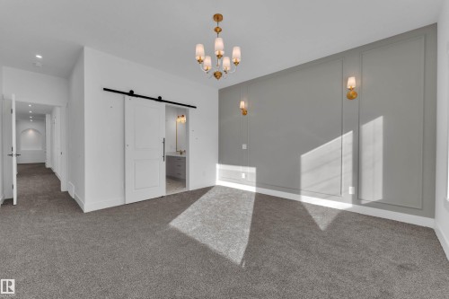Carpeted flooring, decorative wall paneling, gold-tone wall sconces, gold-tone chandelier, and a barn door entry - 226 Linden Loop, Leduc, AB 