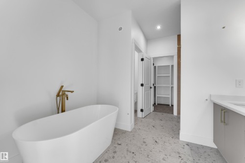 Freestanding soaking tub with a floor-mounted gold-tone faucet, stone-finish flooring, and white walls - 226 Linden Loop, Leduc, AB 