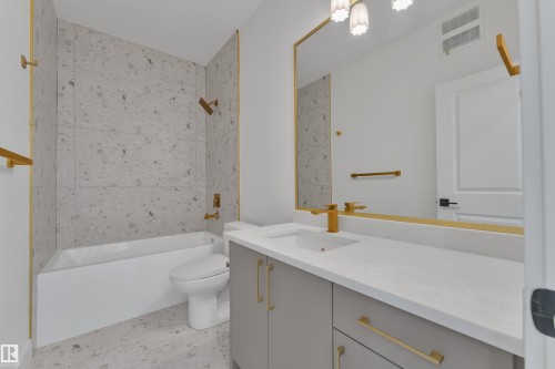 Bathroom featuring a built-in tub with tile surround, a single vanity with an undermount sink, a large mirror with a gold-tone frame, and gold-tone fixtures - 226 Linden Loop, Leduc, AB 