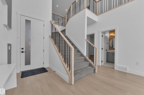 Two-story foyer featuring light wood-finish flooring, a contemporary staircase with wood handrails and black metal spindles, and a modern front entry door with a vertical frosted glass insert - 226 Linden Loop, Leduc, AB 