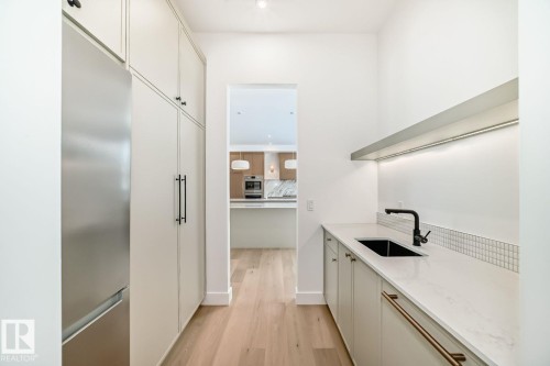 Integrated paneled refrigerator, built-in cabinetry with black hardware, wood-finish flooring, white countertop with undermount sink, and tiled backsplash - 10514 134 Street Nw, Edmonton, AB 
