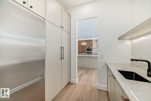 Integrated stainless steel refrigerator, extensive built-in cabinetry, wood-finish flooring, quartz countertop, and black sink with a matching faucet - 10514 134 Street Nw, Edmonton, AB 