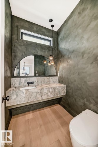 Floating vanity with integrated sink, wood-finish flooring, half-round mirror, rectangular transom window, and three-light pendant fixture - 10514 134 Street Nw, Edmonton, AB 