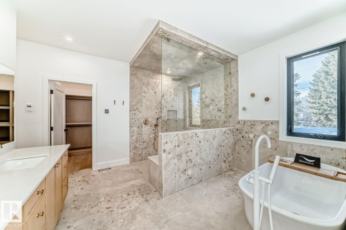Spacious bathroom featuring a freestanding soaking tub, expansive walk-in shower with a built-in bench, dual vanity with a white countertop, and patterned tile flooring - 10514 134 Street Nw, Edmonton, AB 