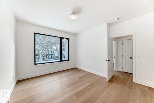 Spacious room featuring wood-finish flooring, a large black-framed window, and a flush-mount ceiling light - 10514 134 Street Nw, Edmonton, AB 