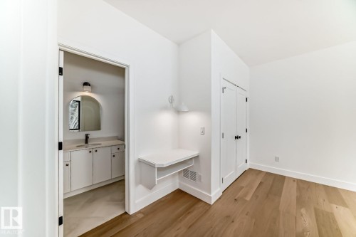 Wood-finish flooring, built-in desk with sconce lighting, white bi-fold closet doors, white vanity with integrated sink, and arched mirror - 10514 134 Street Nw, Edmonton, AB 
