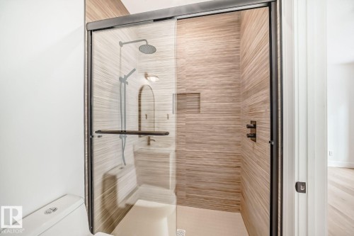 Glass-enclosed shower with a dark-framed door, tile-finish walls, built-in shower niche, and a contrasting rainfall showerhead with a handheld sprayer - 10514 134 Street Nw, Edmonton, AB 