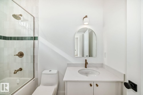 White tiled shower with a green accent band, bronze-finish fixtures, single vanity with a white countertop, and arched mirror - 10514 134 Street Nw, Edmonton, AB 