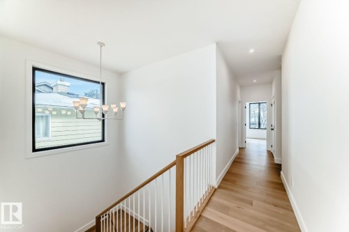 Horizontal window with black trim, modern chandelier, wood-finish flooring, white walls, and a wood handrail with white balusters - 10514 134 Street Nw, Edmonton, AB 