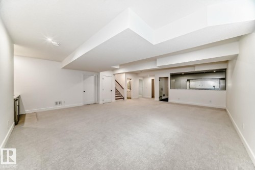 Expansive carpeted area with recessed lighting, integrated wet bar, and a visible staircase with dark wood-finish treads - 10514 134 Street Nw, Edmonton, AB 