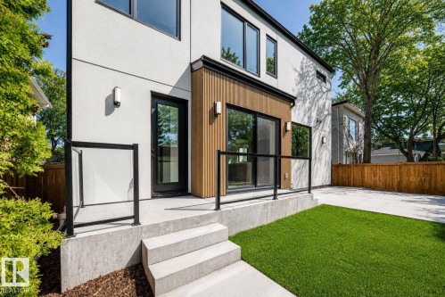 Rear exterior featuring a concrete patio, glass railing, wood paneling, sliding glass doors, and a manicured lawn - 10514 134 Street Nw, Edmonton, AB 