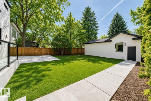 Manicured lawn with a concrete pathway and patio, surrounded by a wood fence, mature trees, and a detached structure - 10514 134 Street Nw, Edmonton, AB 