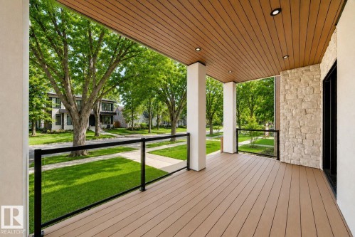 Covered front porch featuring wood-finish decking, stone accent wall, and glass panel railing - 10514 134 Street Nw, Edmonton, AB 
