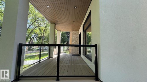 Covered front porch featuring composite decking, glass railing with black posts, and a wood-finish ceiling with recessed lighting - 10514 134 Street Nw, Edmonton, AB 