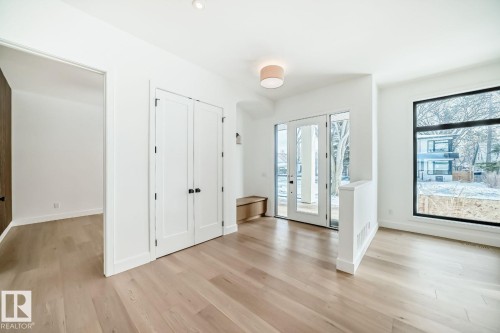 Light wood-finish flooring, white walls, double entry doors with glass panels, large black-framed window, and recessed lighting - 10514 134 Street Nw, Edmonton, AB 