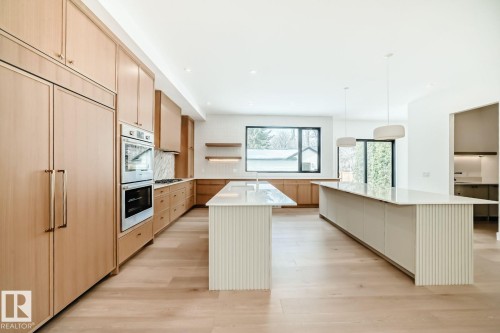 Integrated panel-front refrigerator, double wall oven, wood-finish cabinetry, two kitchen islands with fluted detailing, and light wood-finish flooring - 10514 134 Street Nw, Edmonton, AB 