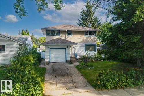 Two-story residence featuring a ground-level garage, front entryway, and a landscaped front yard with mature trees - 14608 93 Avenue Nw, Edmonton, AB 
