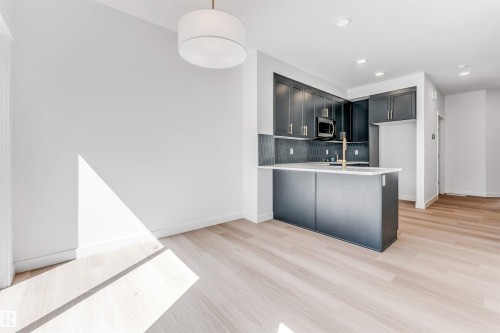 Wood-finish flooring throughout, modern pendant light fixture, recessed lighting, dark flat-panel cabinetry, and a kitchen island with a light-colored countertop - #48 710 Mattson Dr Sw Sw, Edmonton, AB 