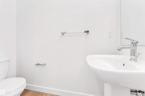 Pedestal sink with chrome faucet, complemented by a white toilet and wood-finish flooring - #48 710 Mattson Dr Sw Sw, Edmonton, AB 