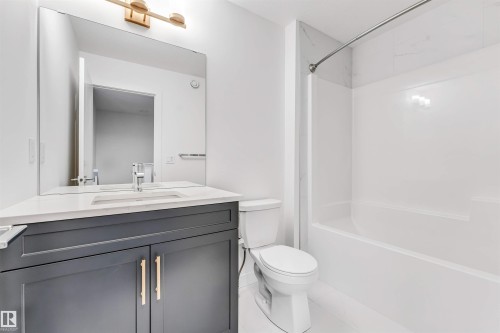 Dark gray vanity with brass-finish hardware, rectangular undermount sink, quartz countertop, and large wall mirror - #48 710 Mattson Dr Sw Sw, Edmonton, AB 