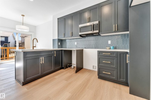 Modern kitchen featuring dark cabinetry with brushed gold hardware, quartz countertops, and a geometric tile backsplash - #48 710 Mattson Dr Sw Sw, Edmonton, AB 