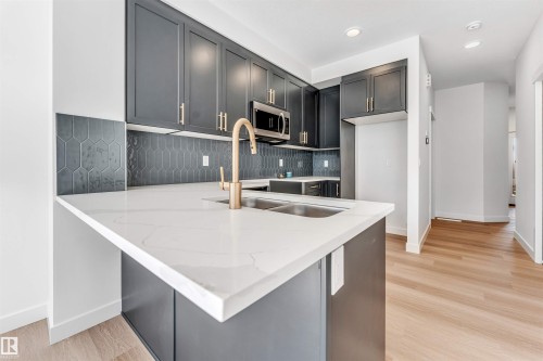 Kitchen island with white stone countertop, dual stainless steel sink, and a gold-finish faucet - #48 710 Mattson Dr Sw Sw, Edmonton, AB 