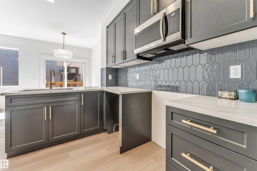 Kitchen featuring dark cabinetry with gold-finish hardware, light countertops, a stainless steel microwave, and an elongated hexagonal tile backsplash - #48 710 Mattson Dr Sw Sw, Edmonton, AB 