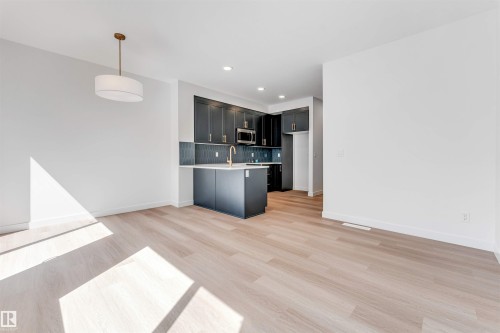 Light wood-finish flooring, recessed lighting, and a kitchen featuring dark cabinetry, stainless steel appliances, and a central island with a gold-tone faucet - #48 710 Mattson Dr Sw Sw, Edmonton, AB 