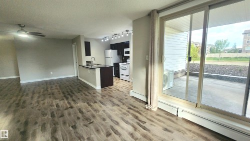 Open-concept living area featuring wood-finish flooring, a ceiling fan, and a kitchen with dark cabinetry - #101 11803 22 Av Sw, Edmonton, AB 