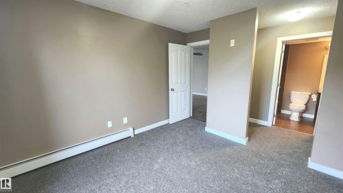 Neutral tone wall paint, grey carpet flooring, white trim, white interior door, and a built-in toilet - #101 11803 22 Av Sw, Edmonton, AB 