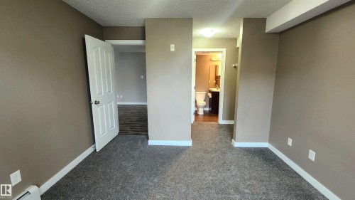 Carpeted flooring, neutral wall paint, white trim, solid core doors, and a bathroom with a vanity and toilet - #101 11803 22 Av Sw, Edmonton, AB 