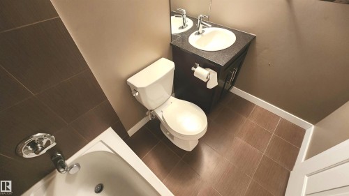 Brown ceramic tile flooring with a coordinated tile bath surround, white porcelain bathtub, and a dark wood-finish vanity with an integrated sink - #101 11803 22 Av Sw, Edmonton, AB 
