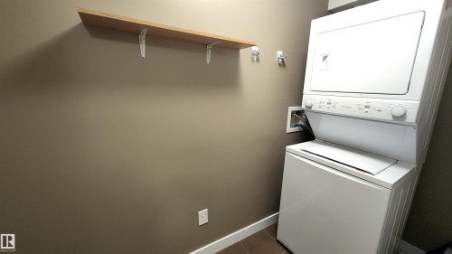 Integrated stacked washer and dryer with a wood-finish shelf and wall hooks for organization - #101 11803 22 Av Sw, Edmonton, AB 