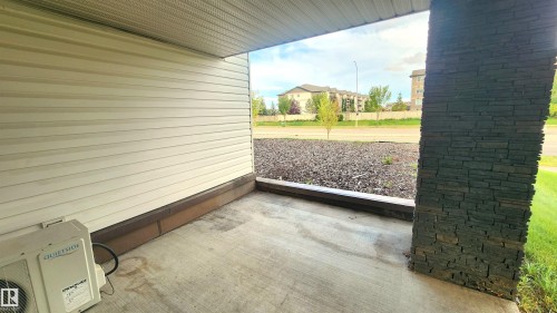Covered concrete patio featuring a stacked stone pillar, horizontal siding, and foundational brick - #101 11803 22 Av Sw, Edmonton, AB 