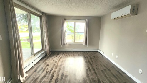 Wood-finish flooring, sliding glass door, additional window, baseboard heating, and a wall-mounted climate control unit - #101 11803 22 Av Sw, Edmonton, AB 