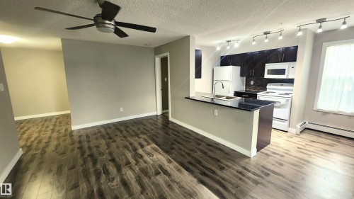Wood-finish flooring throughout, kitchen featuring dark cabinetry, dark countertops, white appliances, and track lighting - #101 11803 22 Av Sw, Edmonton, AB 