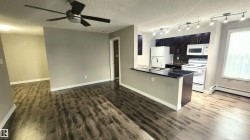 Wood-finish flooring throughout, kitchen featuring dark cabinetry, dark countertops, white appliances, and track lighting - 