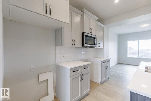 Kitchen featuring light gray cabinetry, white subway tile backsplash, white countertops, and wood-finish flooring - 70 Dansereau Way, Beaumont, AB - Indoor Photo Showing Kitchen