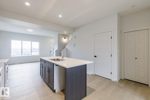 Kitchen island with a double basin stainless steel sink, light countertops, and dark cabinetry - 70 Dansereau Way, Beaumont, AB - Indoor Photo Showing Kitchen With Double Sink