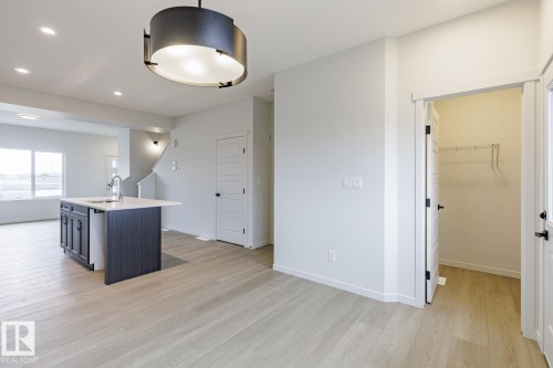Open-concept living space featuring light wood-finish flooring, a kitchen island with dark cabinetry and an integrated sink, a modern pendant light fixture, recessed ceiling lighting, and a staircase with wall sconces - 70 Dansereau Way, Beaumont, AB - Indoor Photo Showing Other Room