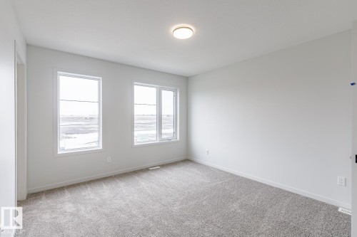 Bright interior room with two large windows, light gray carpeting, neutral wall finishes, and a flush-mount ceiling light fixture - 70 Dansereau Way, Beaumont, AB - Indoor Photo Showing Other Room
