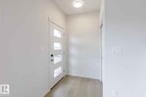 Entryway featuring a white door with four rectangular glass inserts, flush-mount ceiling lighting, wood-finish flooring, and a closet with a white door - 70 Dansereau Way, Beaumont, AB - Indoor Photo Showing Other Room