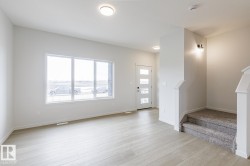 Open-concept living area featuring light wood-finish flooring, a large multi-pane window, and recessed ceiling lighting - 