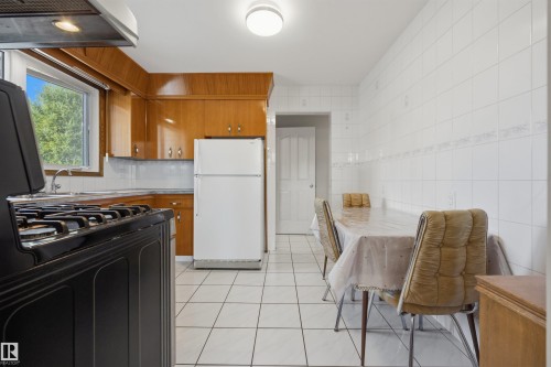 Kitchen featuring wood cabinetry, white tile flooring, tile backsplash, and a built-in range with an overhead exhaust hood - 14008 94 Street Nw, Edmonton, AB 
