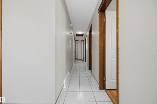 Hallway featuring light gray walls, white square tile flooring, wood-finish door frames, and flush-mounted ceiling lighting - 14008 94 Street Nw, Edmonton, AB 