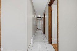 Hallway featuring light gray walls, white square tile flooring, wood-finish door frames, and flush-mounted ceiling lighting - 