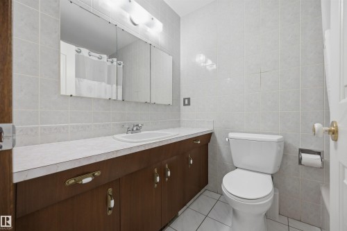 White ceramic tiled walls and flooring with a wood-finish vanity, integrated sink, and triple mirrored medicine cabinet - 14008 94 Street Nw, Edmonton, AB 