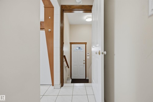 White square floor tiling, light neutral wall paint, wood-finish door frames, white paneled interior doors, and a front entry door with decorative glass inserts - 14008 94 Street Nw, Edmonton, AB 