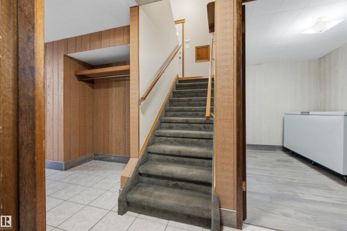 Carpeted staircase with wood-finish handrail, tile flooring, and wood-paneled walls - 14008 94 Street Nw, Edmonton, AB 
