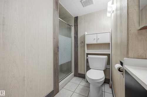 Shower enclosure with glass door, wall-mounted vanity with integrated sink, white toilet, and overhead storage cabinetry - 14008 94 Street Nw, Edmonton, AB 
